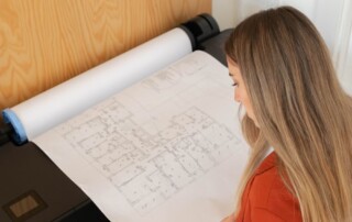 A woman examining architectural blueprints printed using a wide format printer, highlighting the printer's capability to produce detailed large-scale documents.