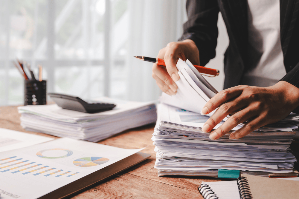 Close up of an office worker sorting through stacks of outputs from a printer, signifying the importance of document management solutions for businesses to stay organized and efficient.