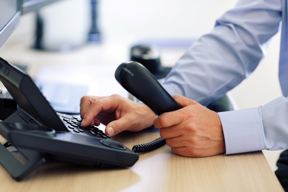 Close up of a businessman making a call on a VoIP phone in an office.